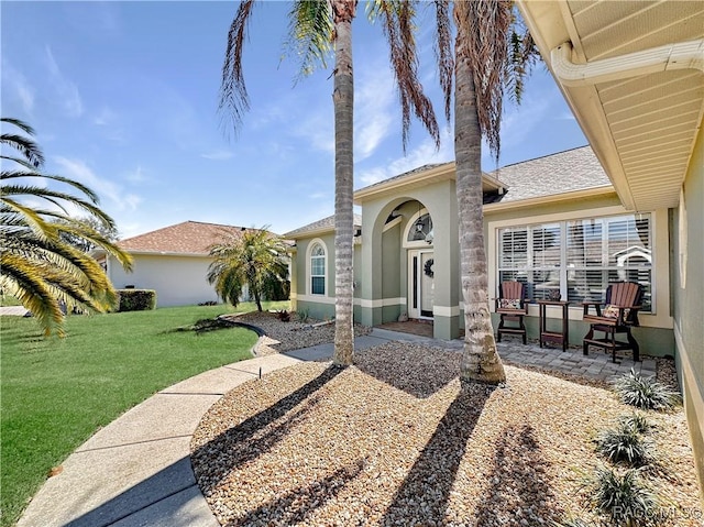 view of front of home with stucco siding, a shingled roof, a patio, and a front yard