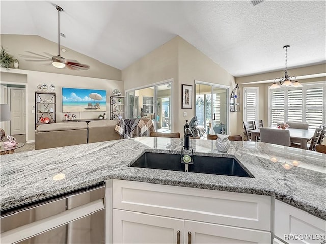 kitchen with lofted ceiling, a sink, white cabinetry, open floor plan, and dishwasher