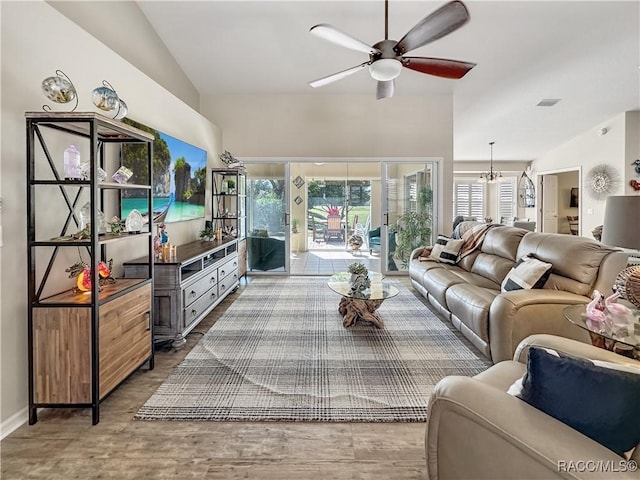 living area with lofted ceiling, ceiling fan with notable chandelier, wood finished floors, visible vents, and baseboards