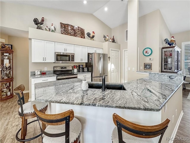 kitchen with light wood-style flooring, a sink, white cabinets, appliances with stainless steel finishes, and a kitchen bar