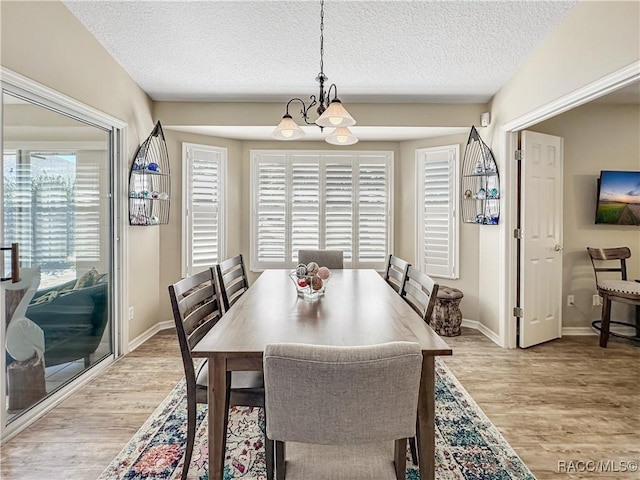 dining space featuring a chandelier, light wood-type flooring, plenty of natural light, and a textured ceiling