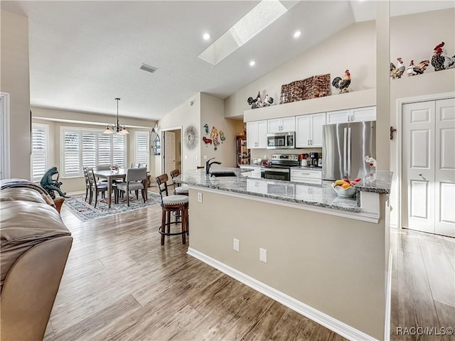 kitchen with stainless steel appliances, visible vents, light wood-style flooring, white cabinets, and a sink