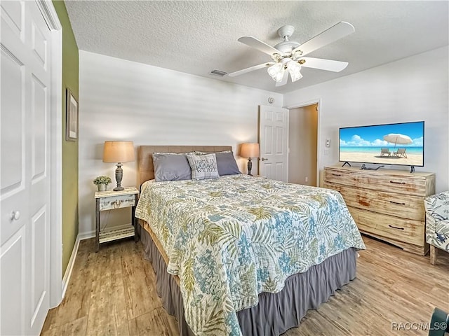 bedroom featuring a textured ceiling, wood finished floors, visible vents, a ceiling fan, and a closet