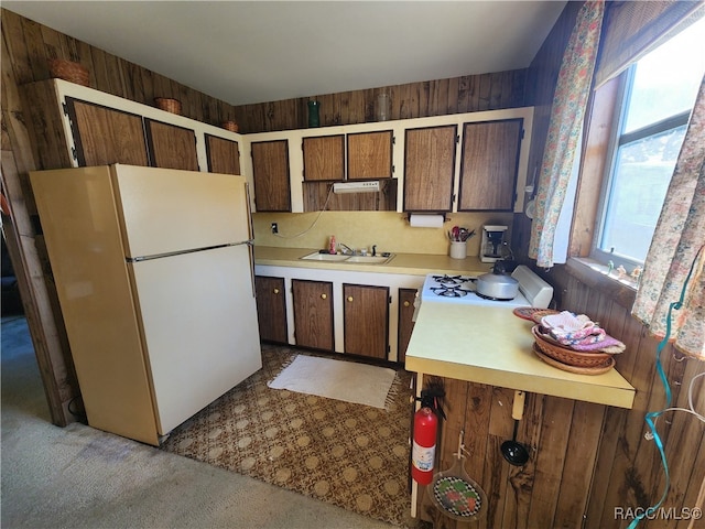 kitchen featuring sink, range hood, white refrigerator, wood walls, and light colored carpet