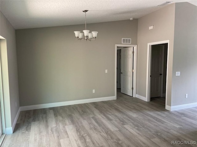 empty room with light hardwood / wood-style flooring, a notable chandelier, vaulted ceiling, and a textured ceiling