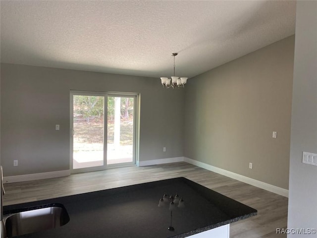 unfurnished dining area featuring hardwood / wood-style flooring, a textured ceiling, and an inviting chandelier