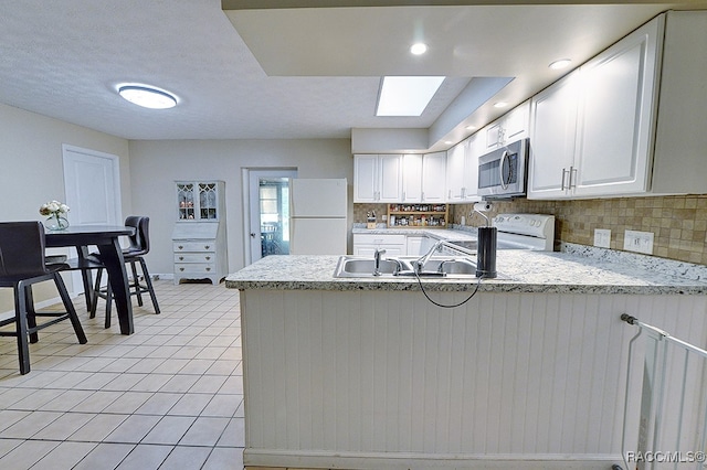 kitchen with a skylight, backsplash, kitchen peninsula, white appliances, and white cabinets