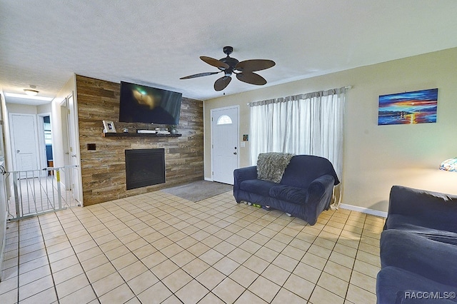 living room with light tile patterned floors, a textured ceiling, a stone fireplace, and ceiling fan