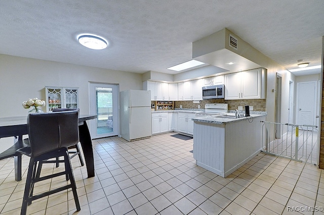 kitchen featuring white appliances, a skylight, white cabinetry, and light tile patterned flooring