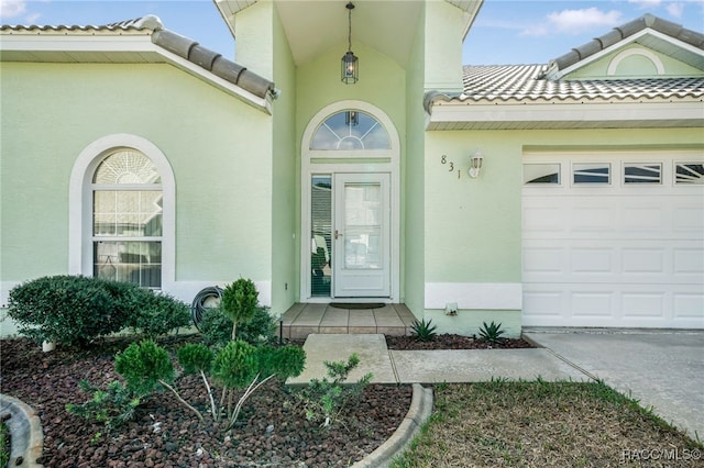 view of exterior entry featuring an attached garage, a tiled roof, and stucco siding