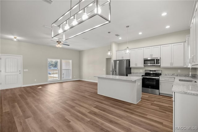 kitchen with sink, appliances with stainless steel finishes, a kitchen island, pendant lighting, and white cabinets