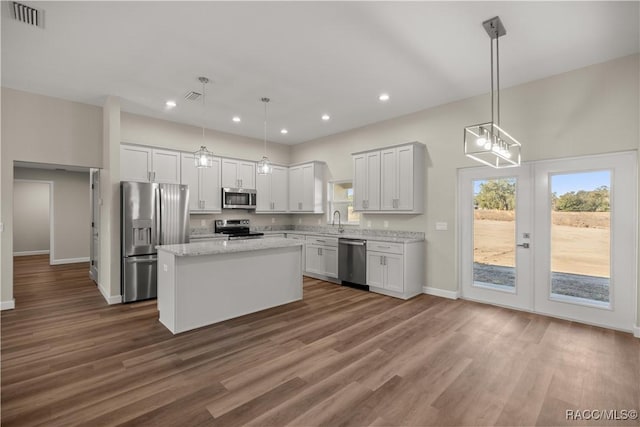 kitchen with stainless steel appliances, a kitchen island, hanging light fixtures, and white cabinetry