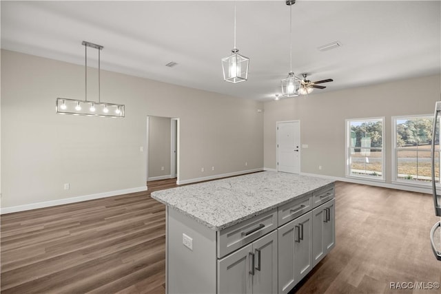 kitchen with hanging light fixtures, dark hardwood / wood-style floors, light stone countertops, and a center island