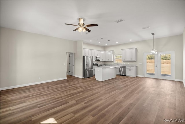 kitchen with appliances with stainless steel finishes, white cabinetry, hanging light fixtures, a center island, and ceiling fan