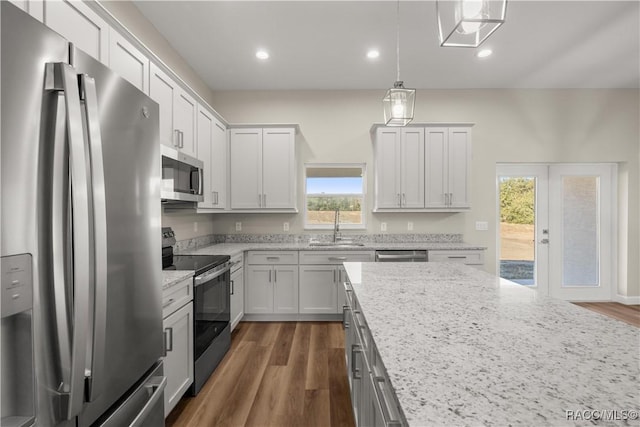 kitchen with sink, stainless steel appliances, light stone counters, white cabinets, and decorative light fixtures