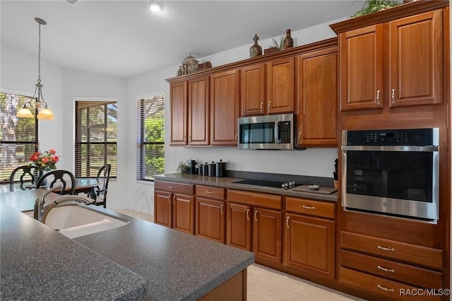 kitchen featuring stainless steel appliances, a sink, hanging light fixtures, brown cabinets, and dark countertops