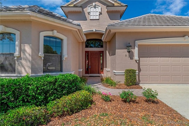 doorway to property featuring a tile roof, an attached garage, and stucco siding