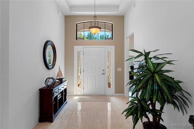 foyer entrance featuring baseboards, a high ceiling, and a tray ceiling