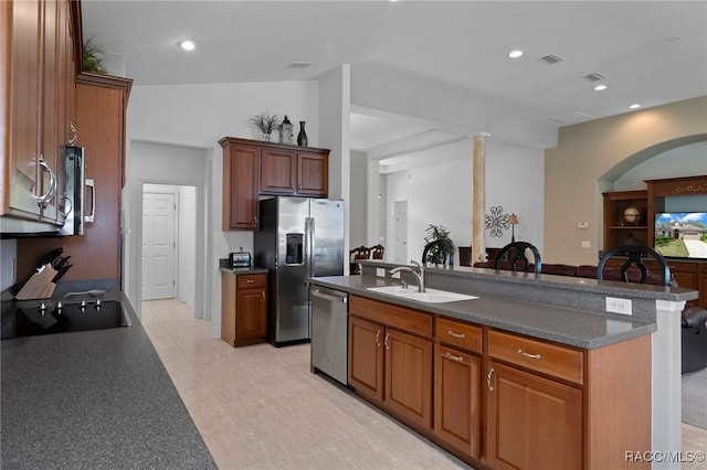 kitchen featuring a sink, visible vents, appliances with stainless steel finishes, dark countertops, and a center island with sink