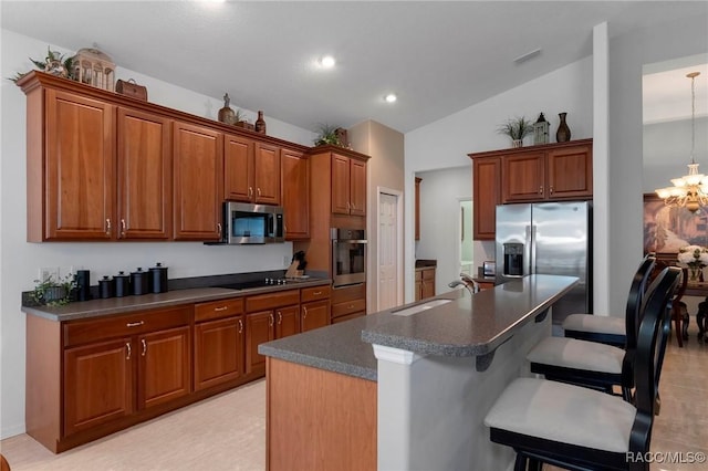 kitchen featuring dark countertops, appliances with stainless steel finishes, a sink, a chandelier, and a kitchen breakfast bar