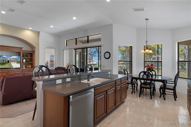 kitchen featuring dark countertops, open floor plan, a sink, dishwasher, and a kitchen bar