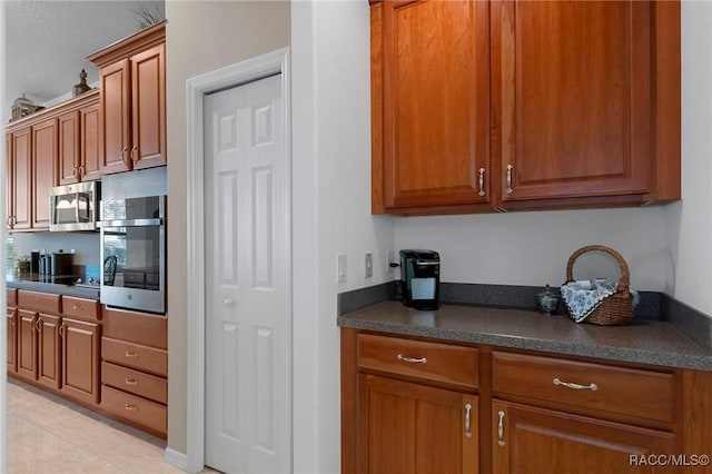 kitchen with dark countertops, brown cabinetry, light tile patterned floors, and stainless steel appliances