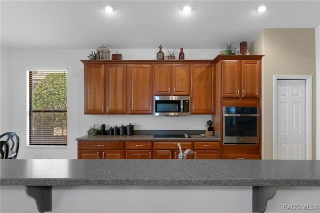 kitchen with stainless steel appliances, dark countertops, brown cabinets, and recessed lighting