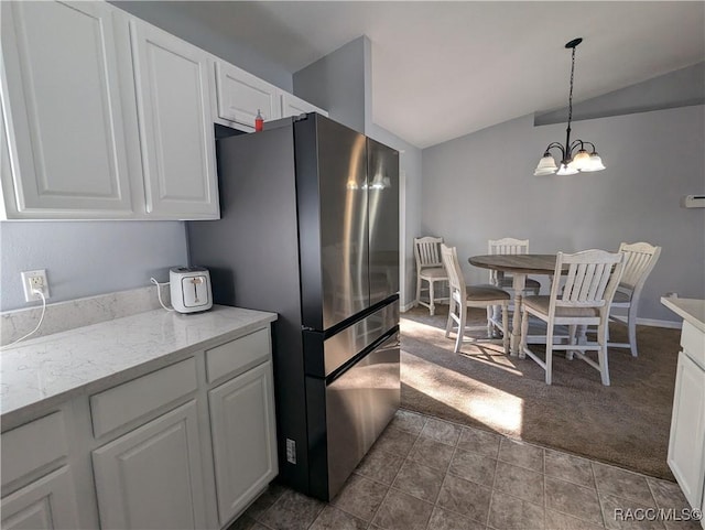 kitchen with an inviting chandelier, stainless steel fridge, white cabinets, and vaulted ceiling