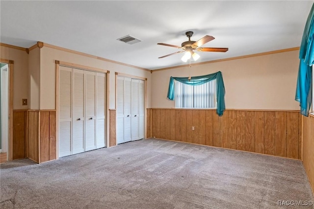 unfurnished bedroom featuring multiple closets, ornamental molding, carpet flooring, and wood walls