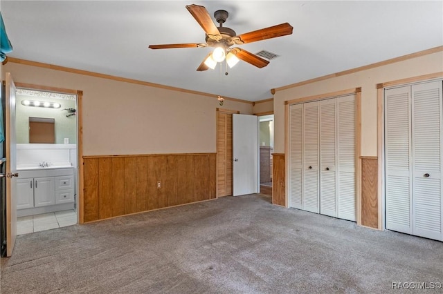 unfurnished bedroom featuring connected bathroom, sink, crown molding, multiple closets, and light colored carpet