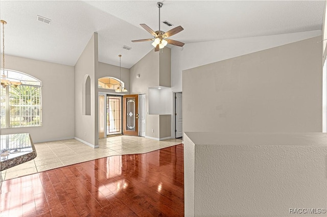 interior space featuring high vaulted ceiling, ceiling fan with notable chandelier, visible vents, and wood finished floors