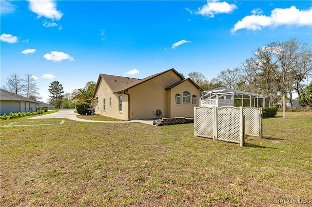 view of side of home featuring glass enclosure, a yard, and stucco siding