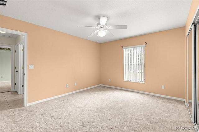 unfurnished bedroom featuring a closet, light colored carpet, ceiling fan, a textured ceiling, and baseboards