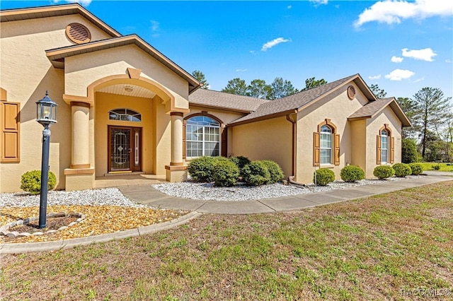 mediterranean / spanish-style home with roof with shingles, a front lawn, and stucco siding