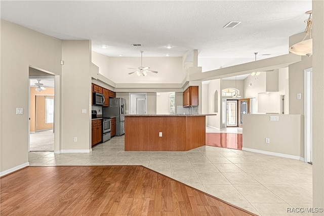 kitchen featuring stainless steel appliances, visible vents, a ceiling fan, open floor plan, and brown cabinetry