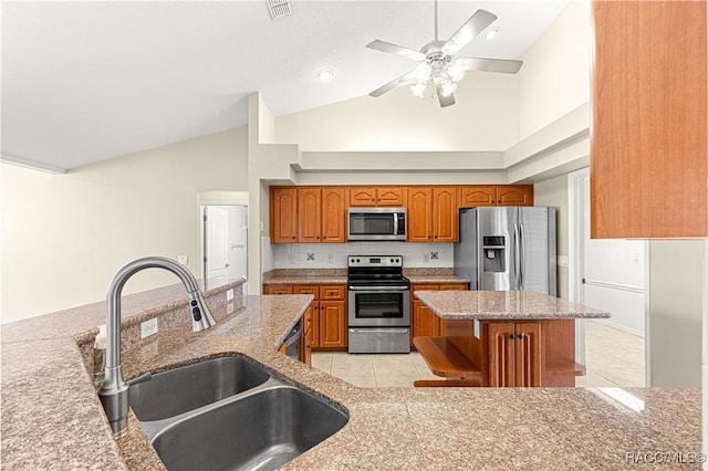 kitchen with a kitchen island, light stone counters, appliances with stainless steel finishes, brown cabinets, and a sink