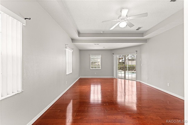 empty room featuring wood-type flooring, a textured ceiling, visible vents, and baseboards