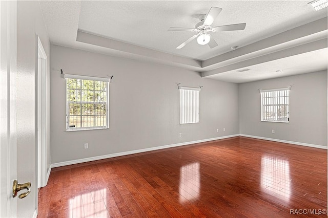 unfurnished room with hardwood / wood-style flooring, visible vents, a tray ceiling, and a wealth of natural light