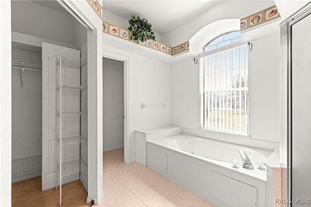 bathroom featuring tile patterned flooring, a spacious closet, and a bath