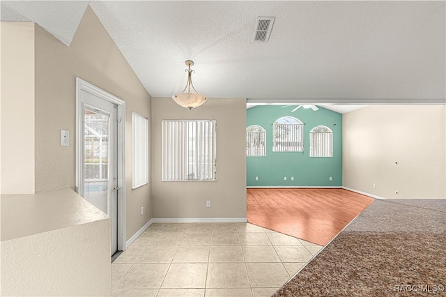 empty room featuring light tile patterned floors, a textured ceiling, visible vents, baseboards, and vaulted ceiling