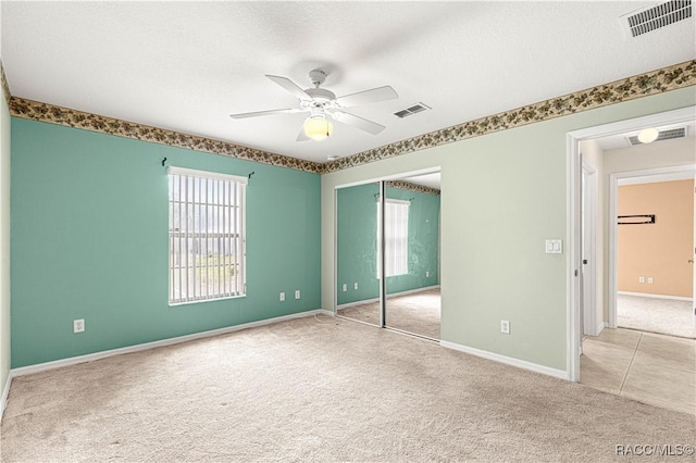 empty room featuring a ceiling fan, a textured ceiling, visible vents, and carpet flooring