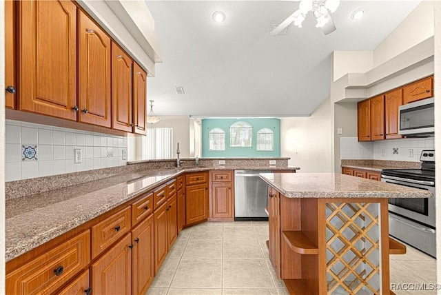 kitchen with light tile patterned floors, light stone counters, brown cabinets, a peninsula, and stainless steel appliances