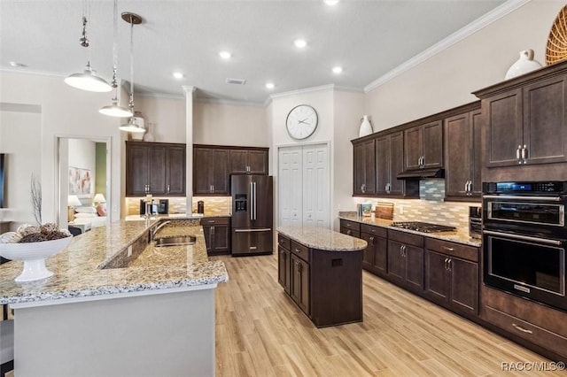 kitchen with crown molding, appliances with stainless steel finishes, a kitchen island with sink, a sink, and under cabinet range hood