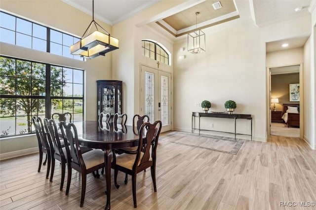 dining space featuring visible vents, baseboards, a towering ceiling, light wood-style flooring, and ornamental molding