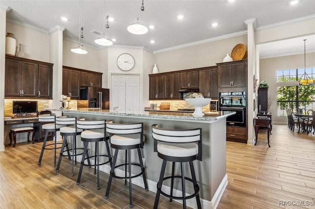 kitchen featuring a breakfast bar area, dark brown cabinetry, dobule oven black, high end refrigerator, and light wood-style floors