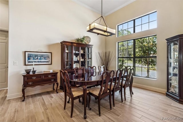 dining area with ornamental molding, a high ceiling, light wood-style flooring, and baseboards