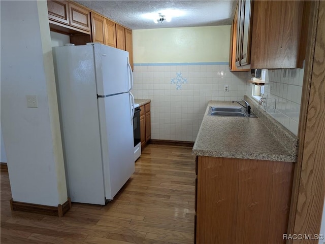 2 Plaza St, Beverly Hills, FL 34465 - kitchen featuring freestanding refrigerator, brown cabinetry, wood finished floors, a textured ceiling, and a wainscoted wall