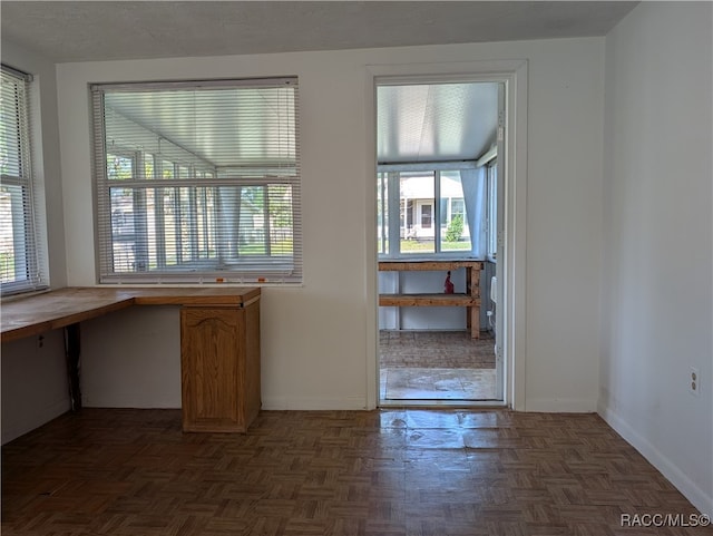 unfurnished office featuring dark parquet floors, a healthy amount of sunlight, built in desk, and a textured ceiling