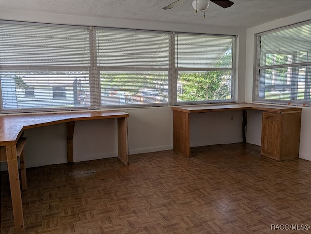 unfurnished office featuring ceiling fan, dark parquet floors, built in desk, and a textured ceiling