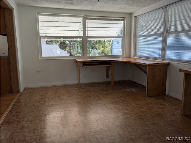 unfurnished office with a textured ceiling, a wealth of natural light, and dark parquet floors